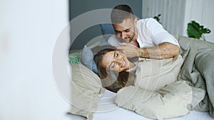 Young beautiful and loving couple wake up at the morning. Attractive man kiss and hug his wife in bed