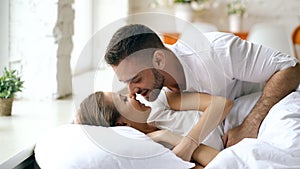 Young beautiful and loving couple wake up at the morning. Attractive man kiss and hug his wife in bed