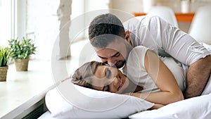 Young beautiful and loving couple wake up at the morning. Attractive man kiss and hug his wife in bed