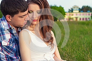 Young beautiful loving happy couple sitting in the box on the grass in the warm evening summer day