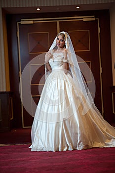 Young beautiful luxurious woman in wedding dress posing in luxurious interior. Gorgeous elegant bride with long veil. Full length