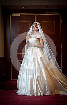 Young beautiful luxurious woman in wedding dress posing in luxurious interior. Gorgeous elegant bride with long veil. Full length