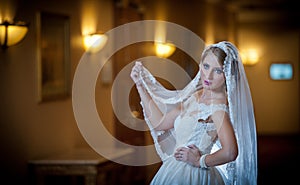 Young beautiful luxurious woman in wedding dress posing in luxurious interior. Gorgeous elegant bride with long veil. Seductive