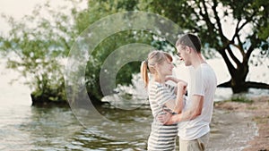 Young beautiful man and woman standing on the beach and talking. Happy couple hugging on the shore of the river.