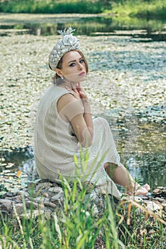 Young beautiful mermaid in seashells crown is sitting on the water background.Mermaid cosplay