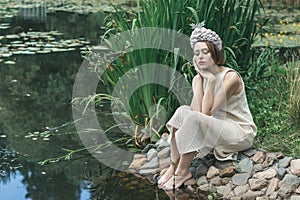 Young beautiful mermaid in seashells crown is sitting on the water background.Mermaid cosplay