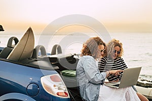 Young and beautiful middle age woman enjoy travel and technology roaming with car and sunset in background - people with laptop