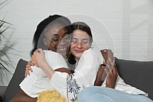 Young beautiful mixed race lesbian couple of black African and caucasian woman sitting on the sofa in their home hugging