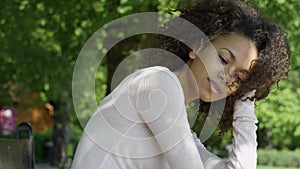 Young beautiful mixed race woman with curly afro hair smiling happily in a green park.