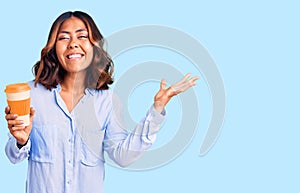 Young beautiful mixed race woman drinking a coffee from take away cup celebrating victory with happy smile and winner expression