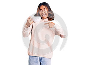 Young beautiful mixed race woman holding a cup of coffee pointing finger to one self smiling happy and proud