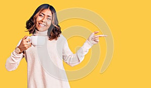 Young beautiful mixed race woman holding a cup of coffee smiling happy pointing with hand and finger to the side