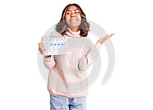 Young beautiful mixed race woman holding travel calendar celebrating victory with happy smile and winner expression with raised