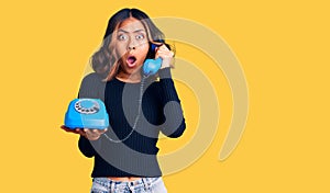 Young beautiful mixed race woman holding vintage telephone scared and amazed with open mouth for surprise, disbelief face