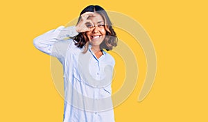 Young beautiful mixed race woman wearing casual business shirt smiling happy doing ok sign with hand on eye looking through