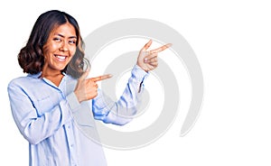 Young beautiful mixed race woman wearing casual business shirt smiling and looking at the camera pointing with two hands and