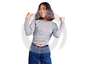 Young beautiful mixed race woman wearing casual clothes very happy and excited doing winner gesture with arms raised, smiling and