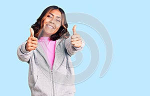 Young beautiful mixed race woman wearing casual sporty clothes approving doing positive gesture with hand, thumbs up smiling and