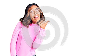 Young beautiful mixed race woman wearing pink shirt smiling with happy face looking and pointing to the side with thumb up