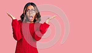 Young beautiful mixed race woman wearing red sweater and glasses celebrating victory with happy smile and winner expression with