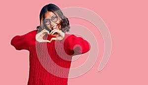 Young beautiful mixed race woman wearing red sweater and glasses smiling in love showing heart symbol and shape with hands