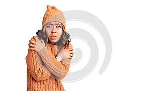 Young beautiful mixed race woman wearing wool sweater and winter hat shaking and freezing for winter cold with sad and shock