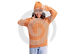 Young beautiful mixed race woman wearing wool sweater and winter hat smiling making frame with hands and fingers with happy face