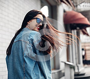 Young beautiful model girl in sunglasses smiles and looks back in the city. Dynamically young girl walks down the street. Hair