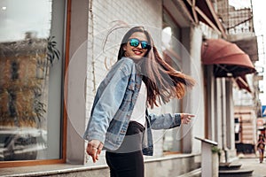 Young beautiful model girl in sunglasses smiles and looks back in the city. Dynamically young girl walks down the street. Hair