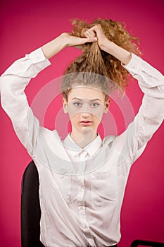 Young beautiful model is putting her thick fair hair into a ponytail.