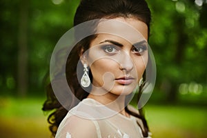 Young beautiful model woman with wedding hairstyle, with expensive earrings and with bright makeup