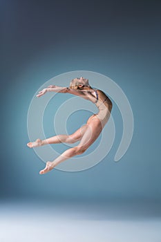 Young beautiful modern style dancer jumping on a studio background