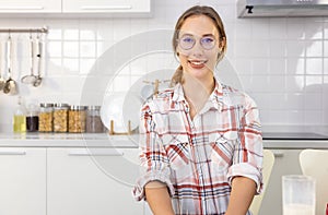 Young beautiful modern woman sitting  near table on kitchen at home