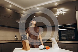 Young beautiful modern woman stands near table on kitchen at home.