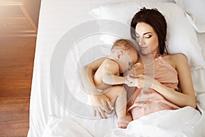 Young beautiful mom breastfeeding her newborn baby lying in bed at home. From above.