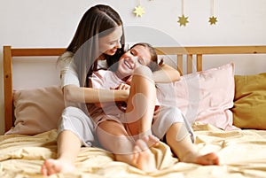 Young beautiful mom with happy little child embracing and expressing love while sitting together on the bed