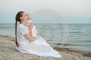 Young beautiful mom sitting on beach and hugging baby. Mothers love and care