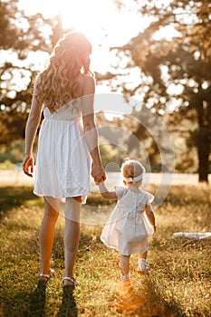 Young beautiful mom is walking with little daughter in the sunny park . The concept of summer holiday outdoors. Mother`s, baby`s