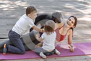 Young beautiful mother with baby son, daughter and with dog exercising and doing yoga at summer park at sunrise