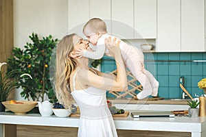 Young beautiful mother is cooking and playing with her baby daughter in a kitchen setting. Healthy food concept