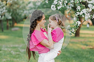 A young beautiful mother is happy and holding her daughter in her arms, they are having fun in the spring park