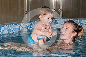 Young beautiful mother and her daughter happy family, play, fool around, and swimming in a pool of blue water, with positive emoti