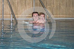 Young beautiful mother and her daughter happy family, play, fool around, and swimming in a pool of blue water, with positive emoti