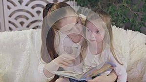 young beautiful mother with her little daughter reading a book sitting on the couch.