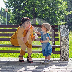 a young beautiful mother and her little daughter sit happy on a bench in the Park and blow soap bubbles