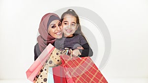 Young beautiful mother in hijab hugs her little daughter, holding shopping bags, smiling, happy family on white