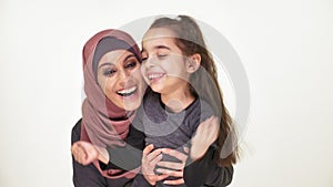 Young beautiful mother in hijab hugs her little daughter, laughing family, happy family concept, idyll, look at camera