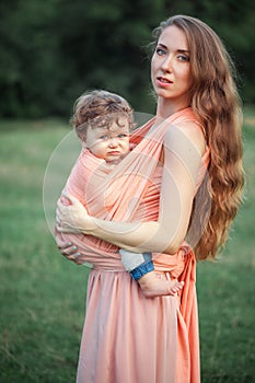 Young beautiful mother hugging her little toddler son against green grass. Happy woman with her baby boy on a summer