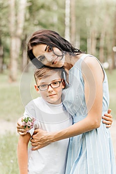 A young beautiful mother hugs her little son during the sunset in nature. Happy family walk in the park