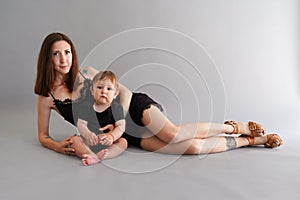 Young beautiful mother in little black dress lying with her son on the floor and taking a foto in studio